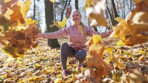 Een aantrekkelijke vrouw in een stadspark gooit herfstbladeren in de lucht. — Stockvideo