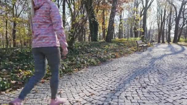 Een meisje loopt langs een kasseistrook in een stadspark. — Stockvideo