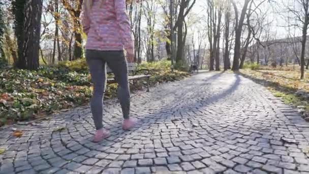 En flicka går längs en kullerstensgränd i en stadspark. — Stockvideo