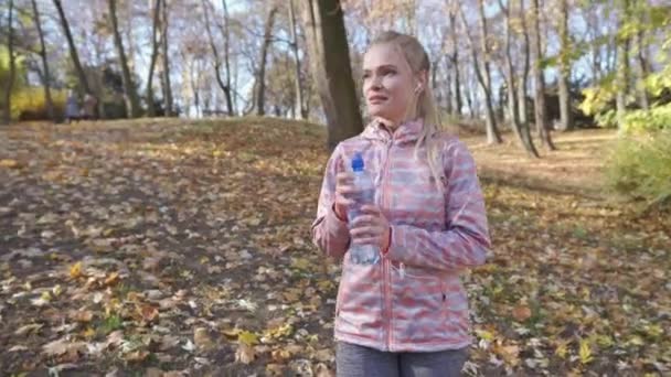 Tijdens het wandelen in een stadspark drinkt een meisje water uit een plastic fles.. — Stockvideo