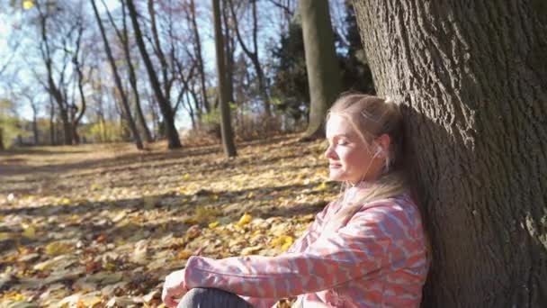 A woman sits by a tree in a city park and rests. — Vídeo de stock