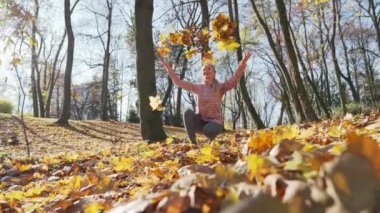 Şehir parkında bir kız sonbahar yapraklarını havaya fırlatıyor..