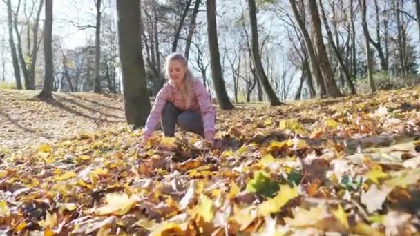 Una donna getta felicemente foglie colorate autunnali in aria. — Video Stock