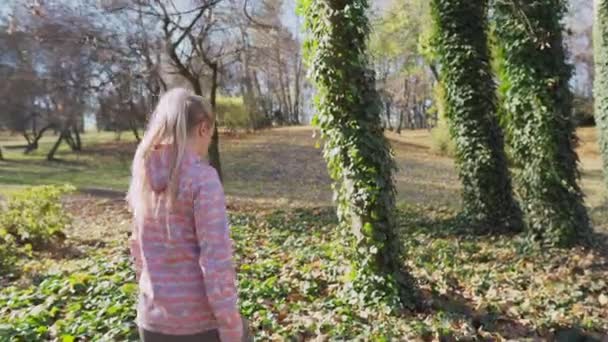 Ein Mädchen nähert sich mit Efeu bedeckten Bäumen beim Gehen. — Stockvideo