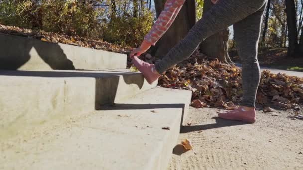 On the steps in the park, a girl stretches her leg muscles. — Video