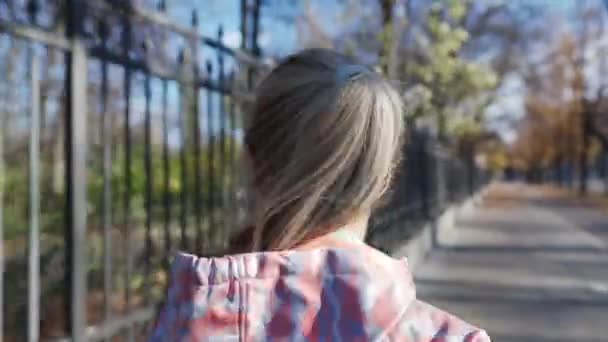 Μια ξανθιά γυναίκα τρέχει λίγο έξω από το φράχτη ενός πάρκου της πόλης.. — Αρχείο Βίντεο