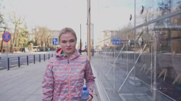 Egy lány sétál a városban egy épület üvegablaka mellett.. — Stock videók