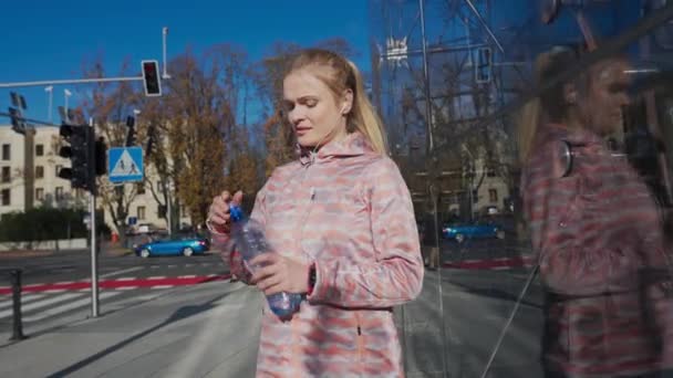 Miközben a városban járkál, egy lány műanyag üvegből iszik vizet.. — Stock videók