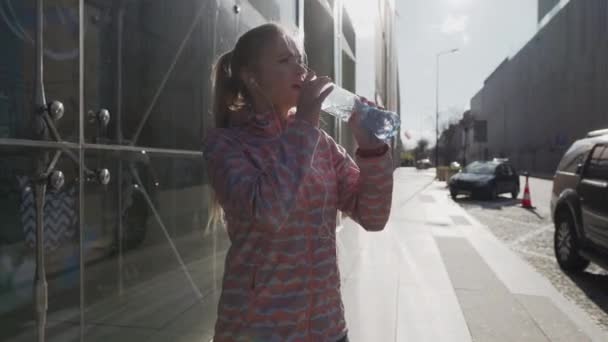 A woman on a walk in the city drinks water from a plastic bottle. — стоковое видео