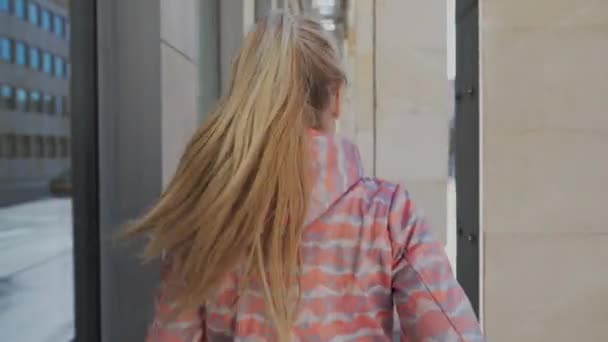 Μια γυναίκα τρέχει σε ένα δρόμο στην πόλη ανάμεσα στις κολώνες ενός κτιρίου.. — Αρχείο Βίντεο