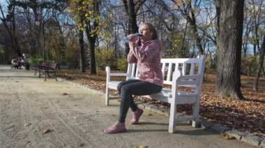 Çekici bir kadın bankta oturur ve plastik şişeden su içer..