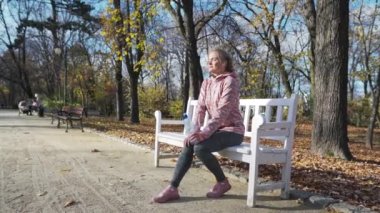 Şehir parkında, genç bir kadın bir bankta dinleniyor ve su içiyor..