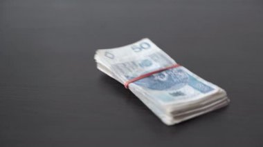 Banknotes tied together with a rubber band fall on the table top.