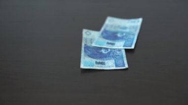 Banknotes of money fall one by one from above onto the table top.