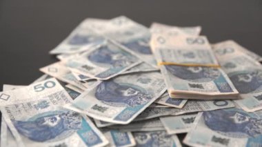 Bundles of packed Polish fifty-zloty bills fall on the loose bills lying around.