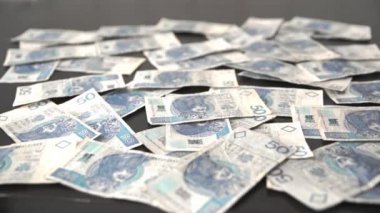 Bundles of packed Polish fifty-zloty bills fall on the loose bills lying around.