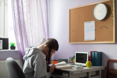 Evde örgü ve gözlüklü bir öğrenci kitap okuyor..