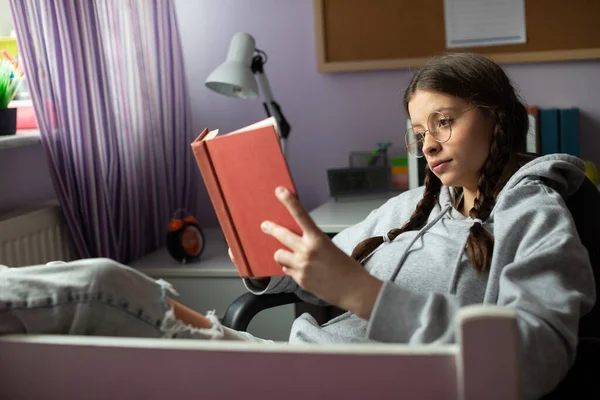 Дівчина-підліток в окулярах читає їй наступне шкільне читання з інтересом . — стокове фото