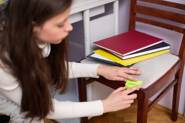 An innovative way to learn English. A teenager sticks a card with the word chair on it. Individualized foreign language learning.