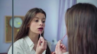 Genç bir kız güzel parlasın diye dudaklarını özel bir fırçayla boyuyor. Uzun ve dağınık saçlı genç esmer..