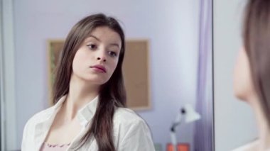 Genç bir kız, saçları açık ve dudakları boyalı bir şekilde nasıl göründüğüne bakar. Saçını kulağına koyar. Uzun ve dağınık saçlı genç bir esmer..