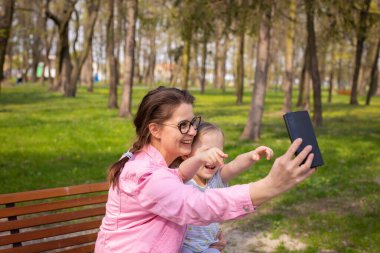Anne ve kızı şehir parkına giderken fotoğraf çekmekle meşguller. Güneşli bir bahar gününde akıllı bir telefonun yardımıyla selfie..