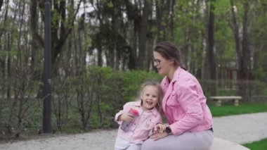 Anne bir davet jesti olarak ellerini onun önünde uzatır. Kız kızını öpüyor ve kaldırıyor. Şehir parkında güneşli bir bahar günü.