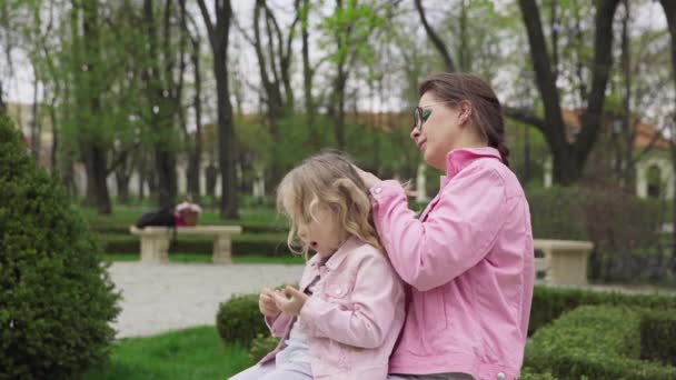 Няня Сидит Скамейке Маленькой Девочкой Попечении Молодая Мать Заплетает Своим — стоковое видео