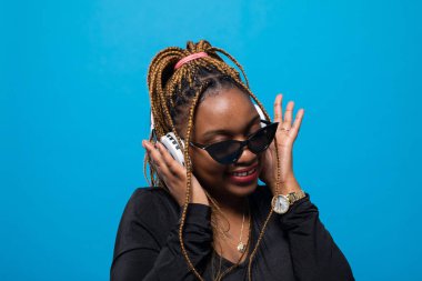 Tatmin olmuş koyu tenli bir kız kablosuz kulaklıkla müzik dinliyor. Kafası hafifçe eğik. Müzik dinlerken odaklanmış.