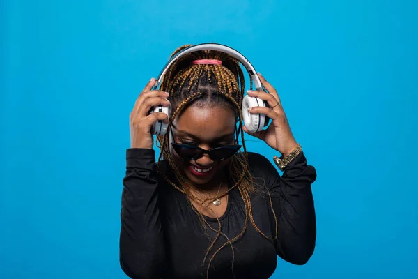 A girl with dark complexion puts on headphones and will listen to music. Dark-skinned young woman with many braids.