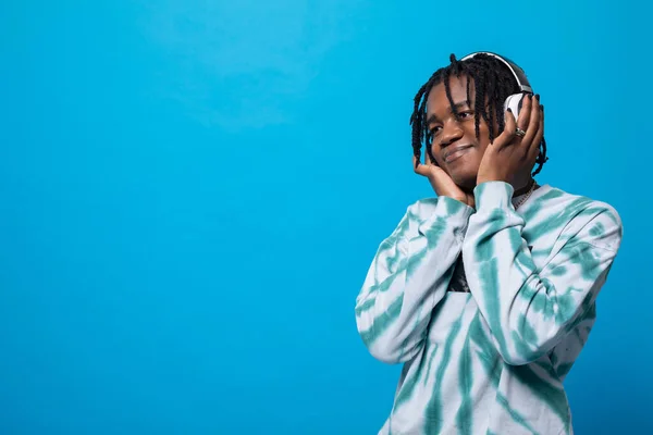 A dark-skinned man listens to music on wireless headphones. A student with short hair in dreadlocks. A smiling young man.