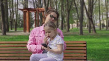 A mothers love for her daughter. A parent kisses her child. Relaxing and resting on a bench in a city park. A sunny spring day outdoors.