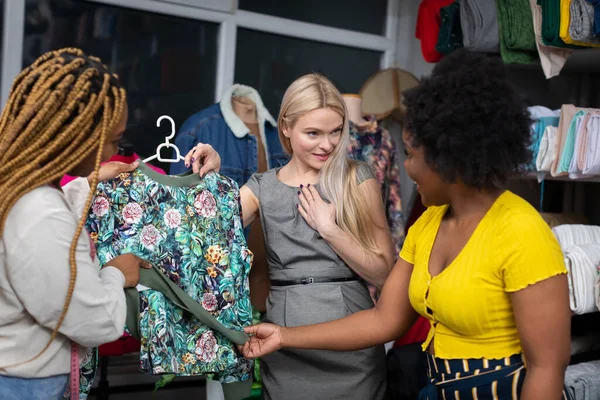 Two dark-skinned shopkeepers show a blouse to a new customer and tell her that this blouse is perfect just for her. A store and a tailors store.