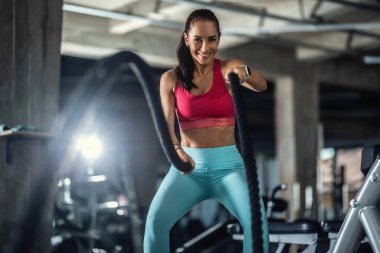 Kavisli ip kullanan bir kadın spor salonunda çalışıyor, gülümsüyor..