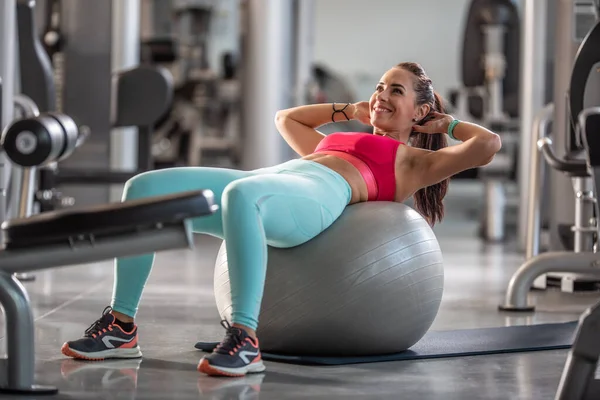 Vrouw Sportkleding Doet Crunches Een Fitnessbal Omringd Door Trainingsapparaten Sportschool — Stockfoto