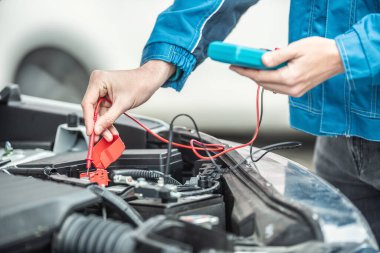 Araba elektrikçisi ya da tamirci arabanın motor içindeki aküyü açık kaputla kontrol ediyor..