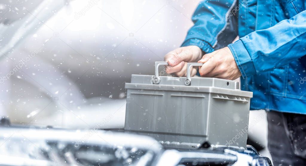 Car technician replaces dead car battery in winter conditions. 