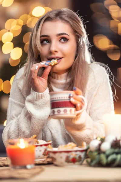 美しい若いですブロンド女性味新鮮なクリスマスジンジャーブレッドで偉大な味を保持カップの束茶またはコーヒー — ストック写真