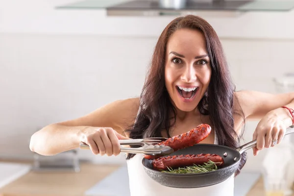 兴奋的女人从有厨房用具的锅里取出烤香肠 — 图库照片