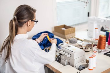 Örgü makinesinin yanındaki kadın el yapımı giysi atölyesindeki kıyafetleri ölçüyor..