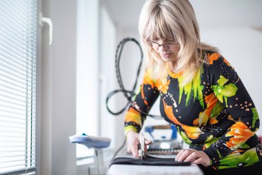 Kadın terzi kendi atölyesinde kumaşı makasla kesiyor..