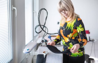 Terzi atölyesinde çalışan kadın elindeki siyah kumaş parçasına bakıyor..