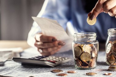 Bir elinde bir banknot tutan ve hesap makinesi olan bir cam kavanoza 50 sent koyan kadının ayrıntıları..