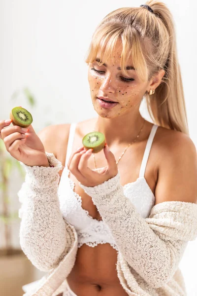 Hermosa Joven Rubia Sienta Lencería Blanca Cama Con Aplicación Kiwi — Foto de Stock