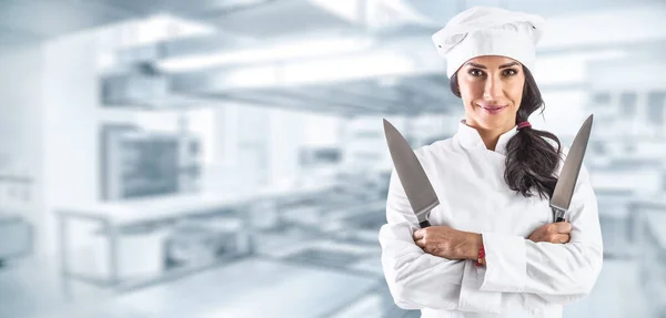 女厨师双手叉腰站在餐馆厨房里 手里拿着两把锋利的小刀 — 图库照片