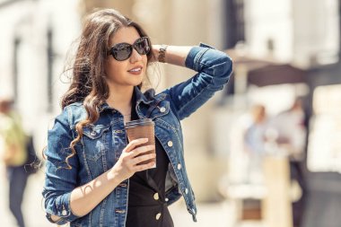 Kahveli genç bir kadın şehrin sokaklarında yürüyor..