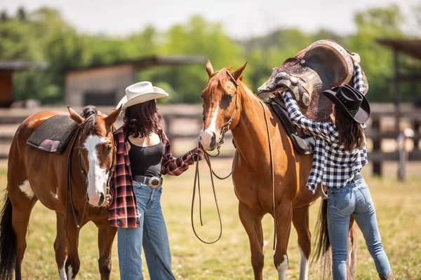 Dwie Przyjaciółki Pomagające Sobie Nawzajem Odsunąć Siodło Konia Letniej Przejażdżce — Zdjęcie stockowe