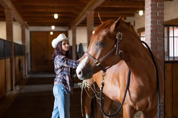 Młoda Dziewczyna Kowbojskim Kapeluszu Grzebie Stajennego Konia Który Spogląda Jej — Zdjęcie stockowe