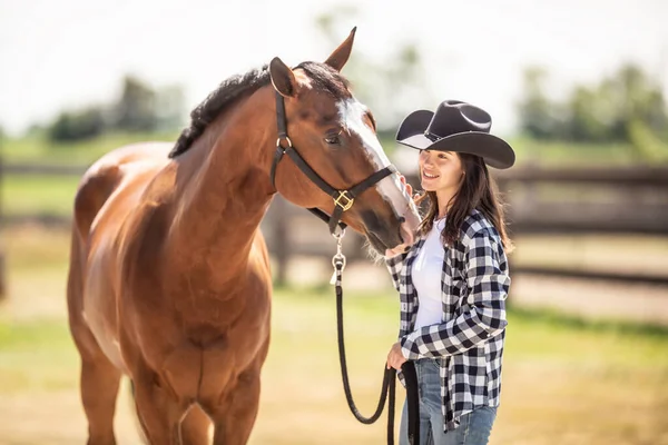 A bond between a horse and a young woman in cowboy hat on a ranch outdoors.