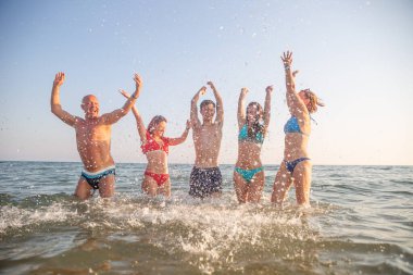 A family of five enjoys a vacation together. They jump for joy on the seashore.